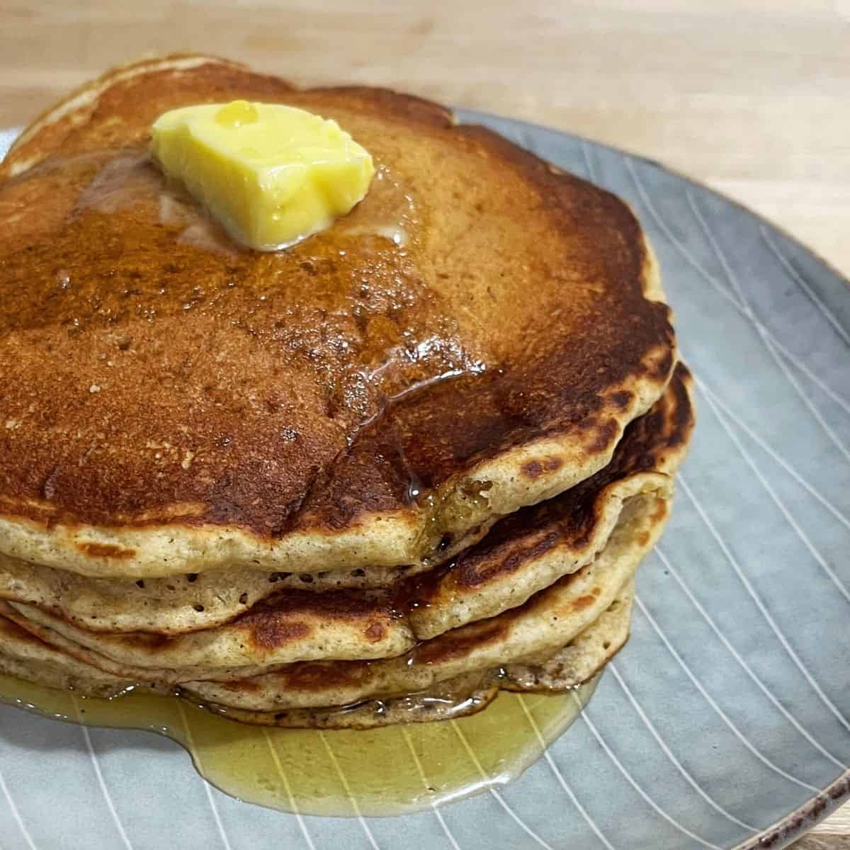 A stack of three whole wheat banana pancakes with a pat of butter and maple syrup.