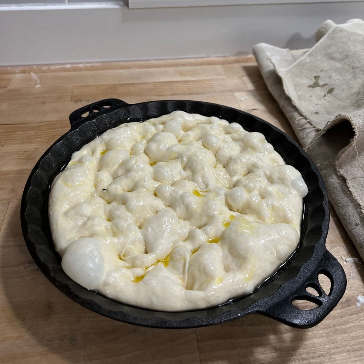 Dimpled focaccia dough in cast iron pan.