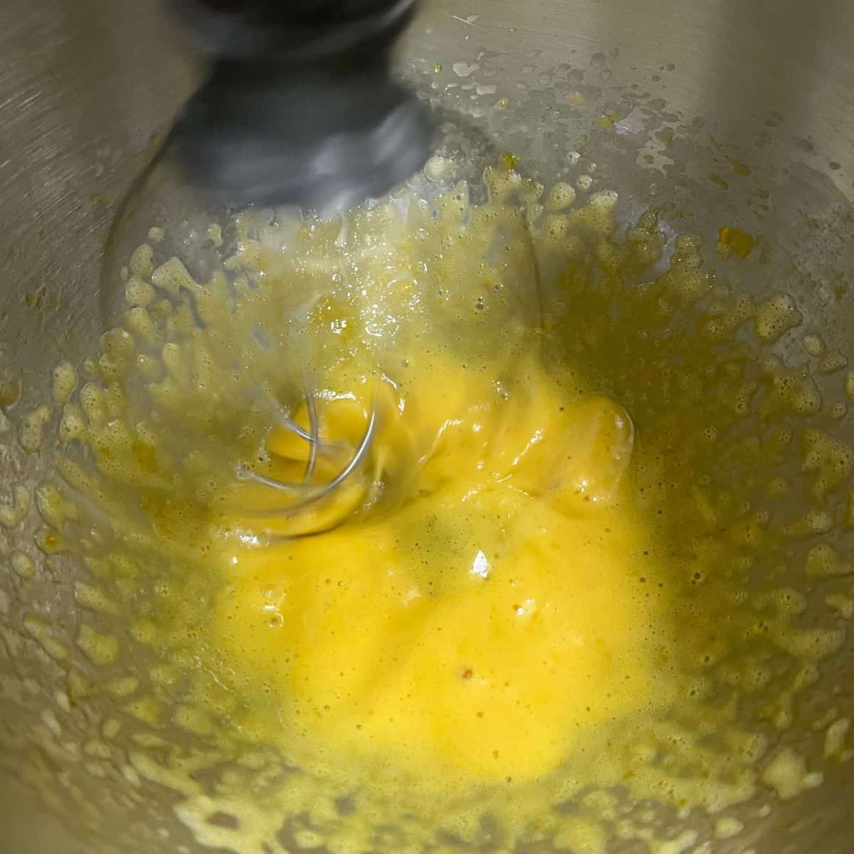Yolk, mustard, salt and vinegar looking frothy in a a KitchenAid bowl with whip attachment.