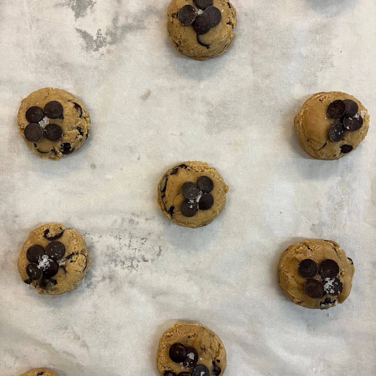 Cookie dough on a tray topped with chocolate coins and sea salt.