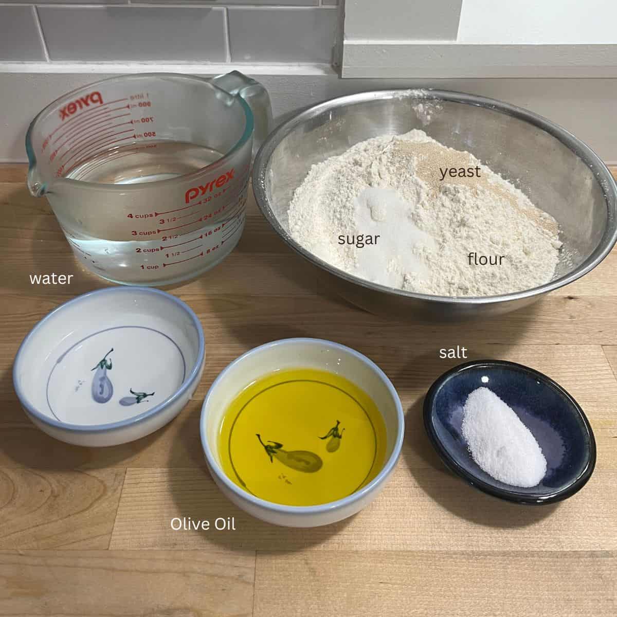 Two bowls of water, olive oil, salt and a bowl with flour, sugar and yeast.