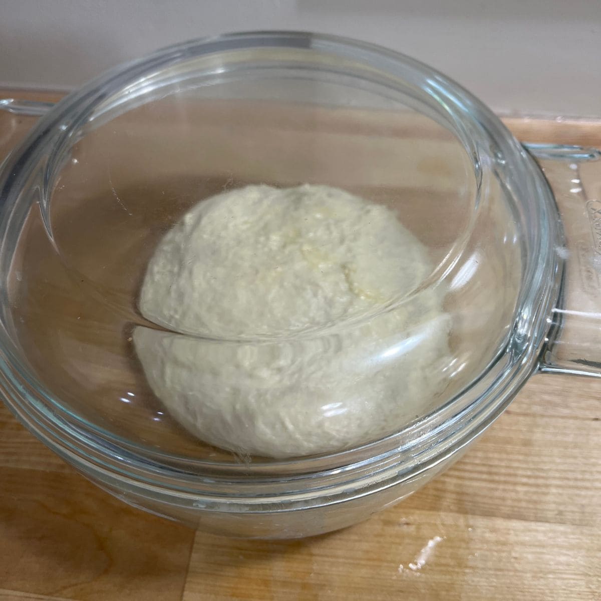 Focaccia dough in a glass container, covered.
