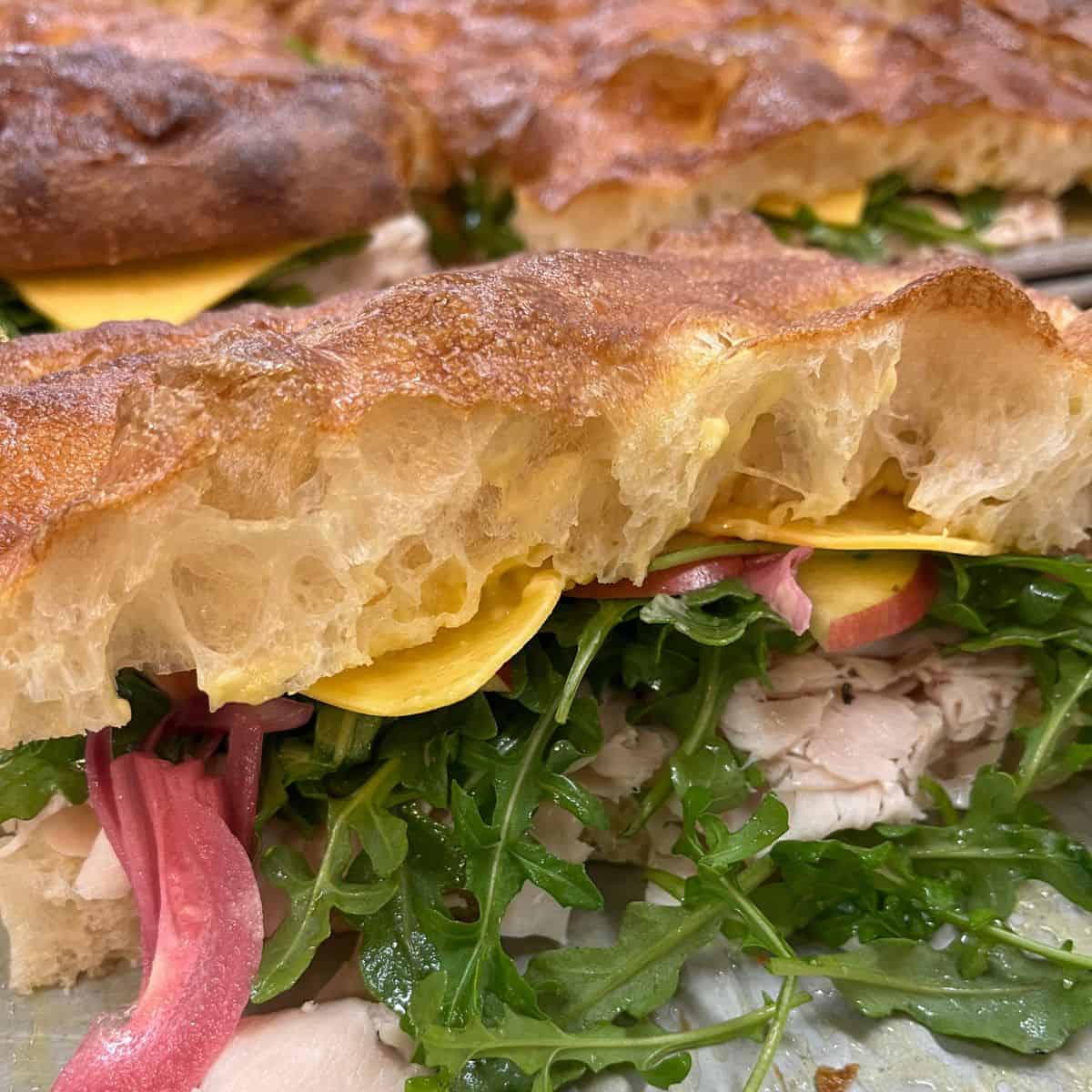 Close up of turkey, cheddar, pickled onions, arugula and apples sandwiched between focaccia.