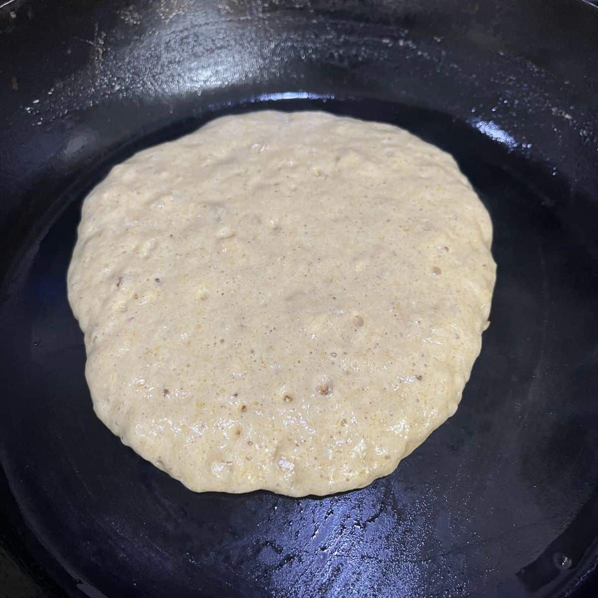 A pancake in a frying pan, just before flipping with noticeable bubbles.