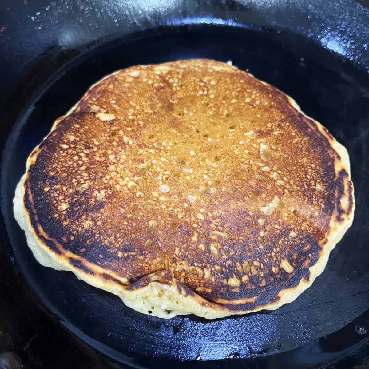 A golden-brown pancake after flipping in pan.