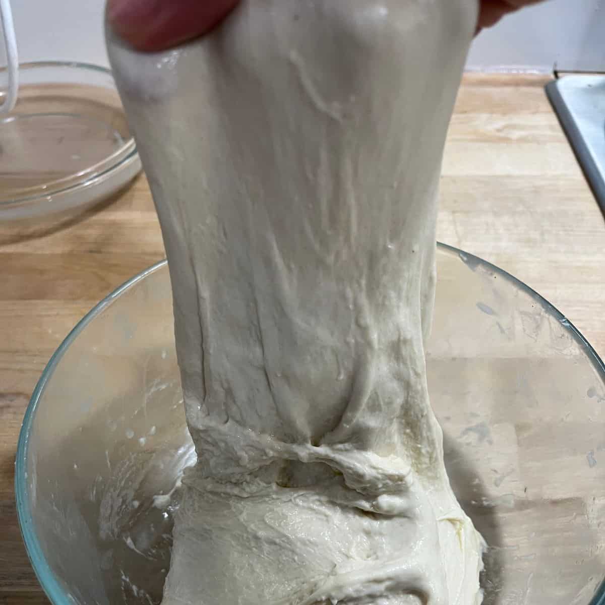 Stretching focaccia dough in glass bowl.