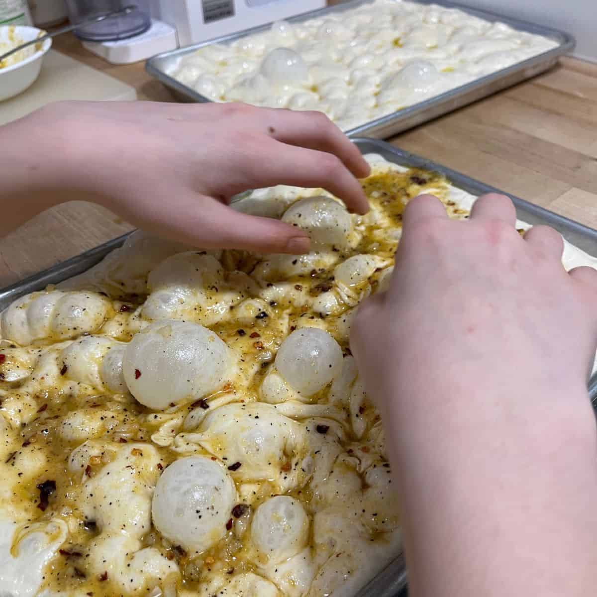 Two hands and a bubbly focaccia dough to show how to dimple.