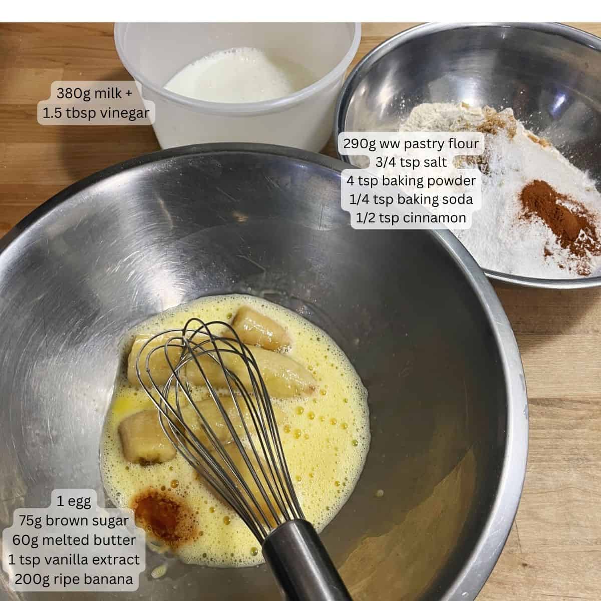 A bowl with a whisked egg, banana, vanilla and melted butter. A second bowl with whole wheat flour, brown sugar, cinnamon, baking power, baking soda and salt. A third container with milk + vinegar.