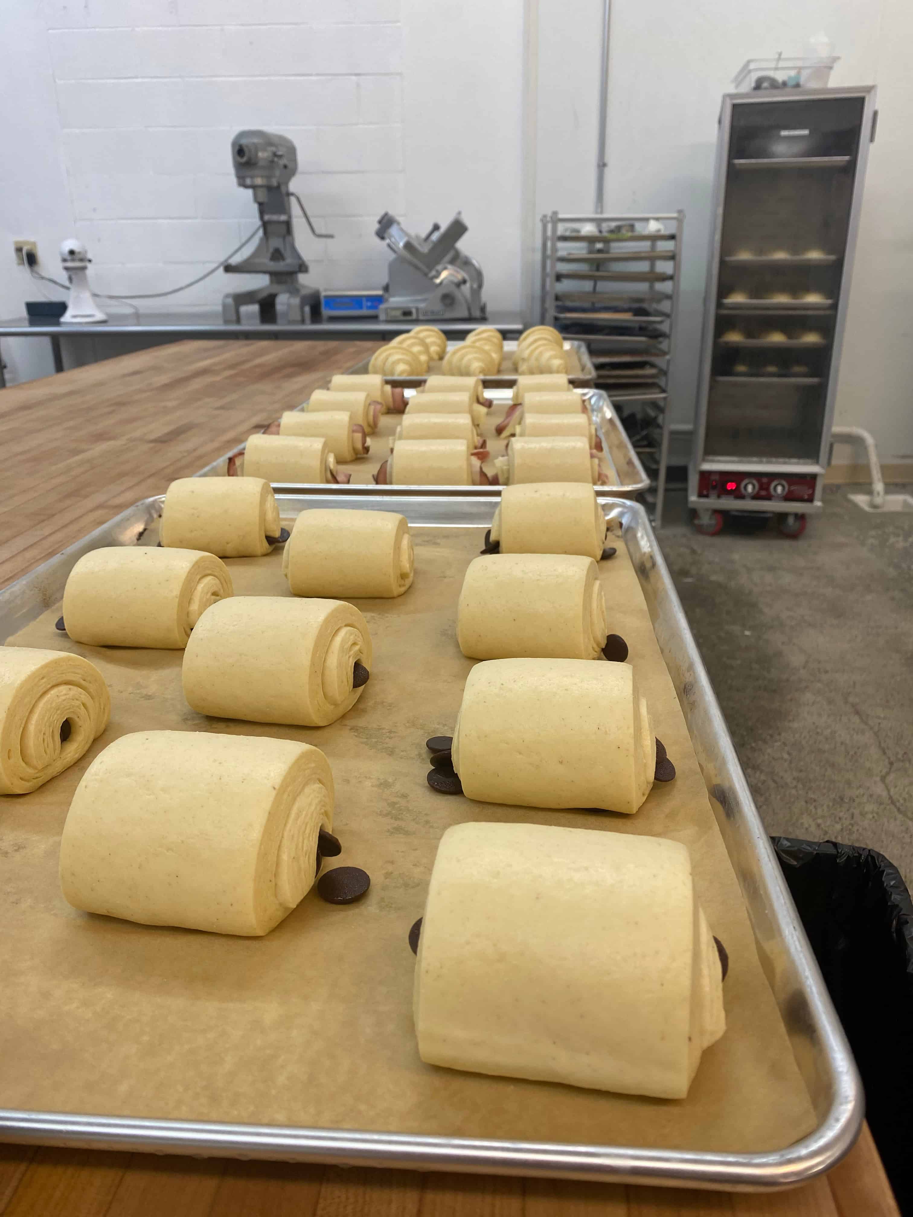 Trays of croissants on a table with equipment in the background.