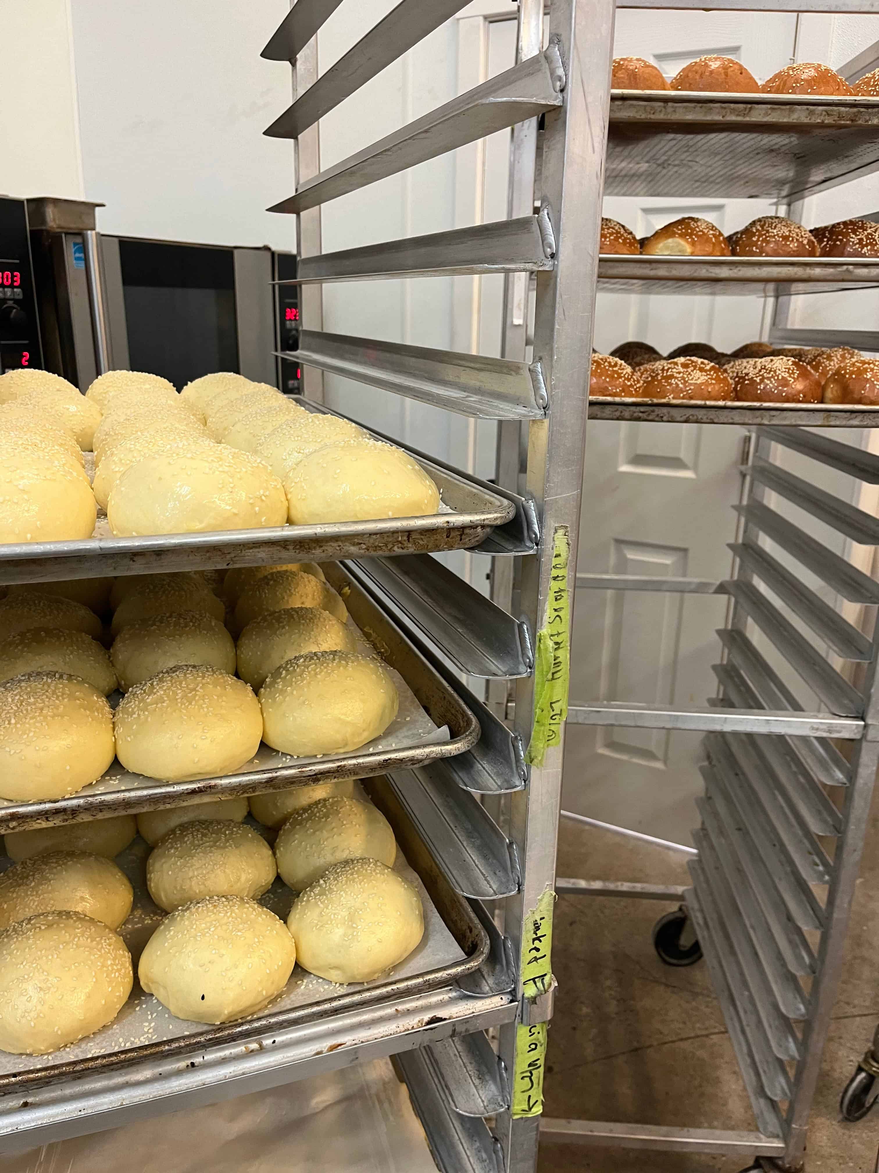 Rolls proofing on a rack next to  rack of baked rolls.
