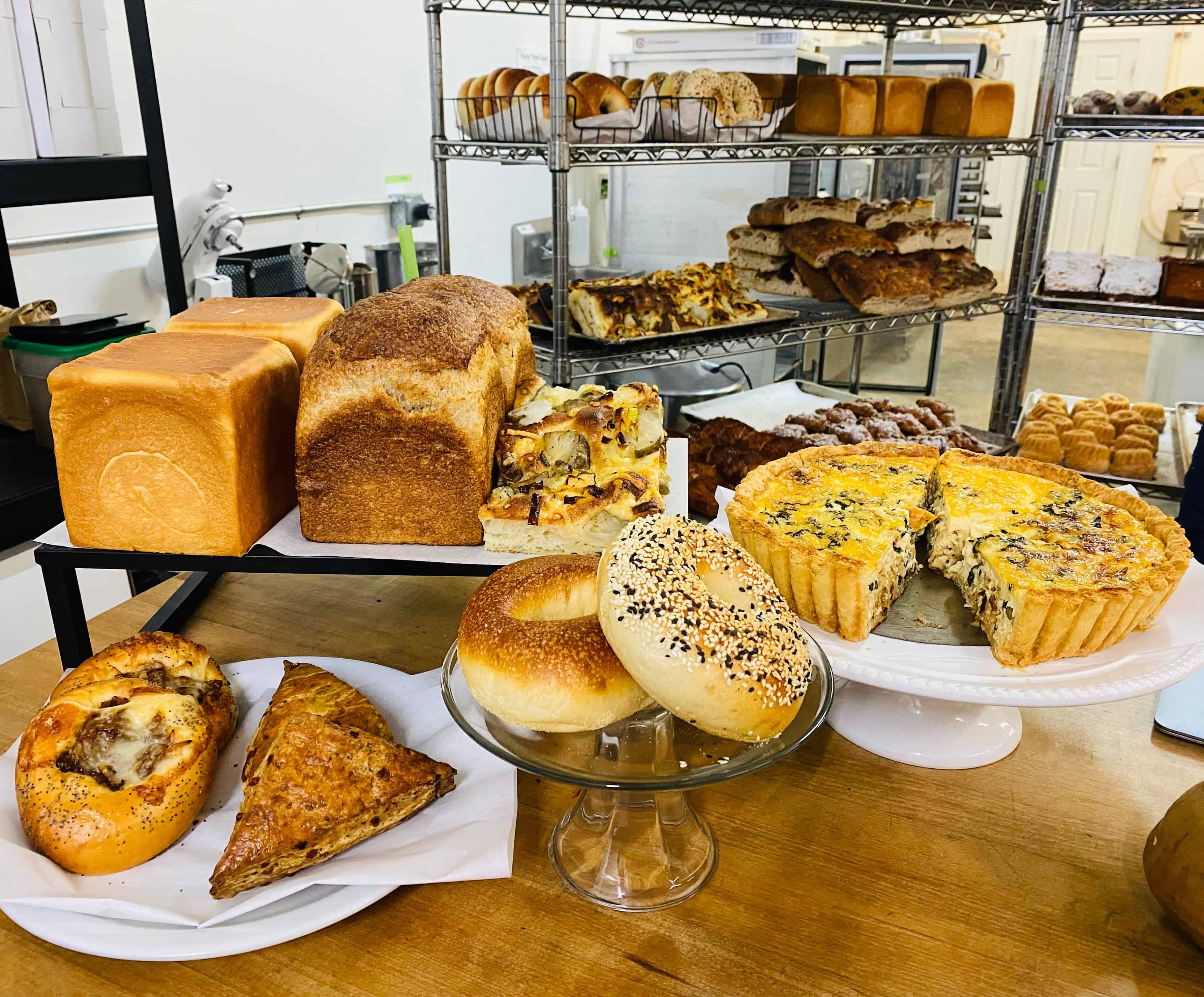 Pastries, and bread on a counter.  Bread and pastries on the shelves in the background.