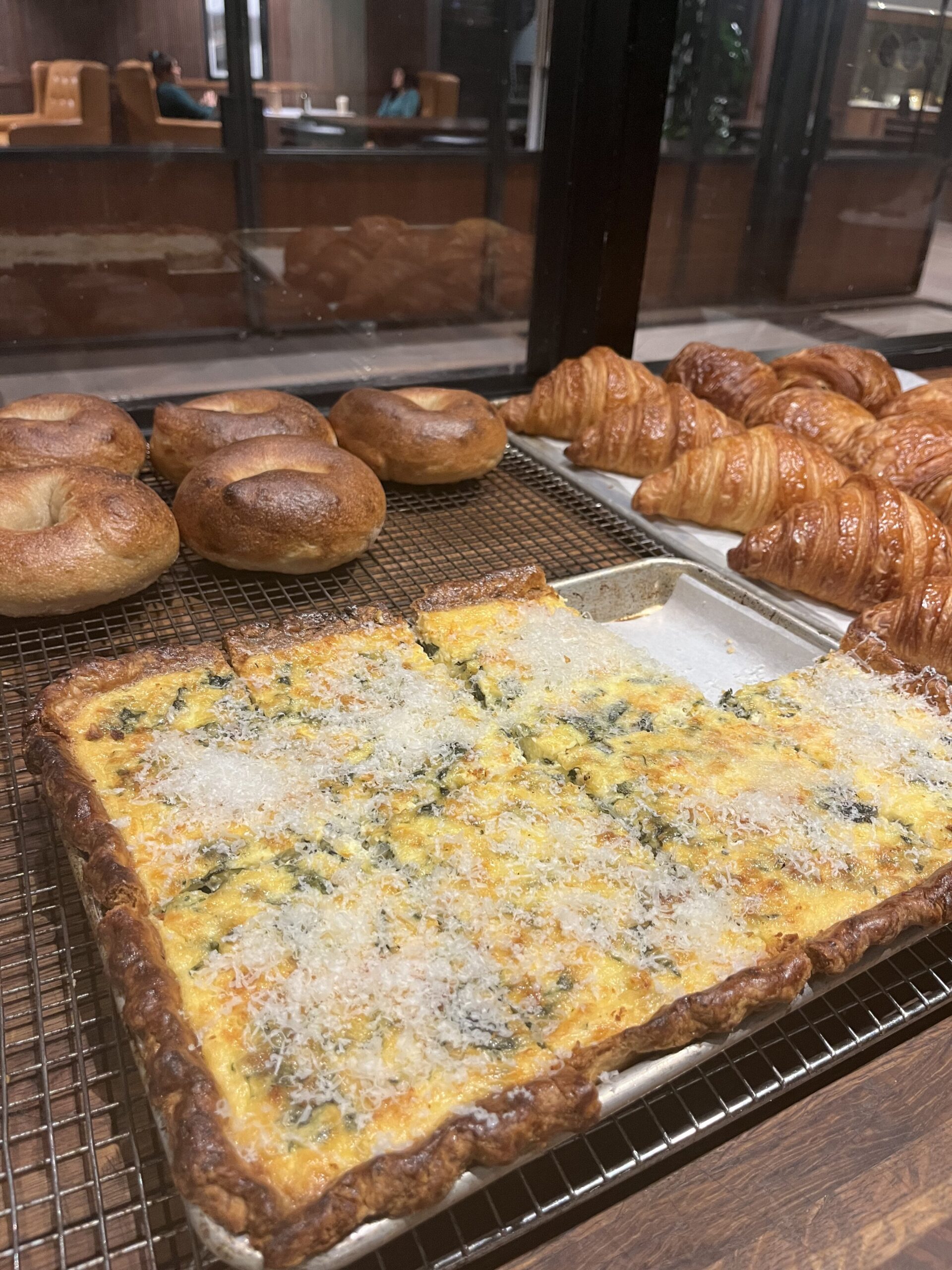rectangular quiche on display along with bagels and croissants