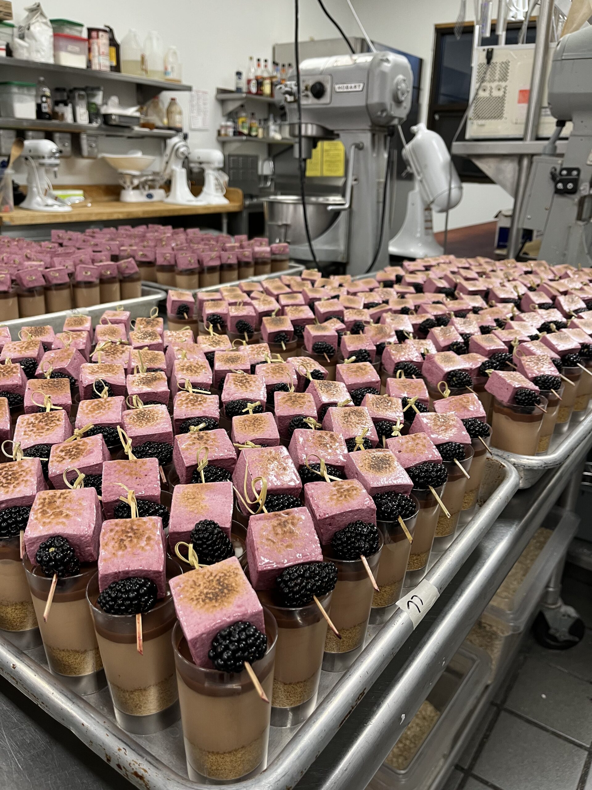 Hundreds of chocolate mousse cups topped with ganache and blackberry and marshmallow skewer garnish.