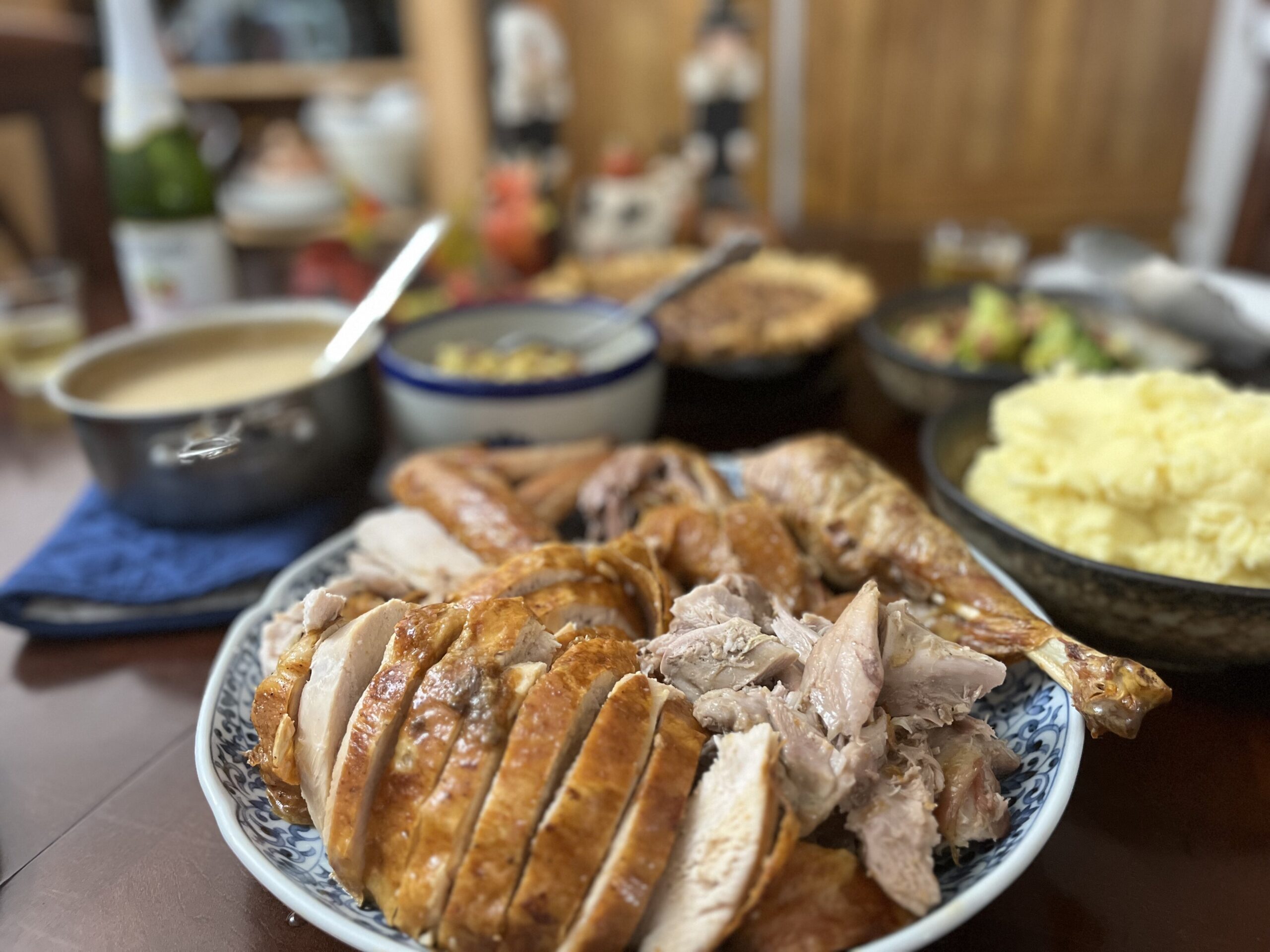 Thanksgiving table - turkey in foreground. mashed potatoes, roasted vegetables, stuffing, gravey and pie in the background.
